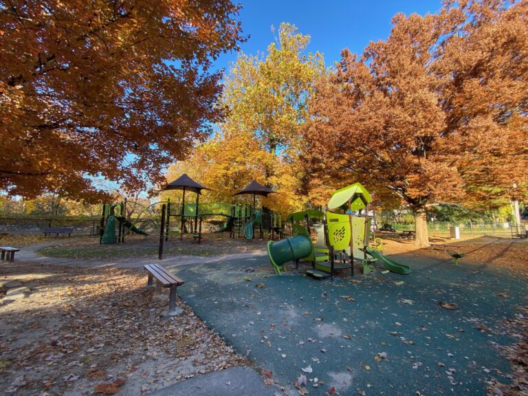 Hastings-on-Hudson playground surrounded by peak autumn foliage on a clear fall day
