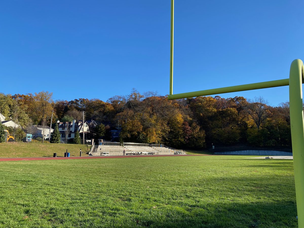 Houses on a wooded hillside in fall color above an athletic field and bleachers