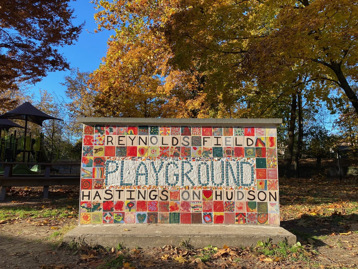 Colorful mosaic tile sign reading Reynolds Field Playground, Hastings-on-Hudson, in front of autumn trees